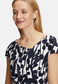 Robe à motif floral avec un design bleu marine et blanc, un décolleté arrondi et des manches courtes, fabriquée en tissu lisse.