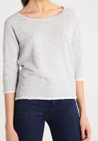 Maglietta a righe grigia chiara in maglia con scollatura a barca e maniche a tre quarti. Presenta un orlo grezzo per una vestibilità rilassata. Realizzata in tessuto morbido.