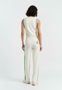 Top senza maniche bianco lavorato a maglia con accenti colorati sulle spalle, abbinato a pantaloni bianchi con strisce laterali verdi e rosa e una grafica di cartone animato.