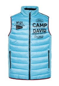 Blau gepolsterte Weste mit hohem Kragen, Frontreißverschluss und Seitentaschen. Verfügt über schwarze Schriftzüge und Logos sowie rote Akzente am Saum. Strapazierfähiger Stoff.