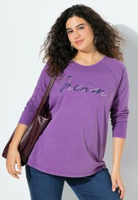 Fialový dlouhý rukáv s kulatým výstřihem a stříbrným nápisem "POJĎME SNÍT," v kombinaci s tmavě modrými džíny a burgundskou kabelkou.