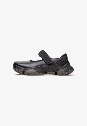 Black Mary Jane-style shoe with a textured strap, minimalist design, flexible rubber sole, and a smooth leather upper.