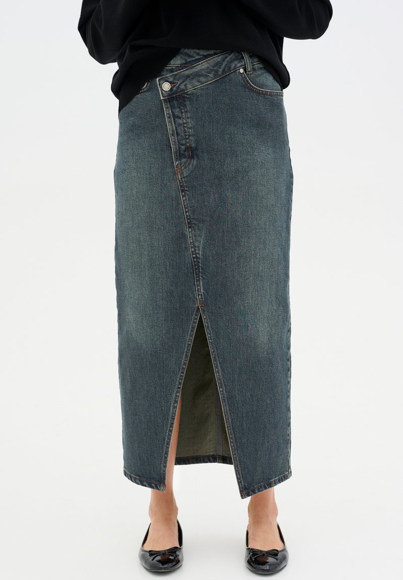 Denim maksi krilo v temno modri barvi z sprednjim razporkom, ki ima visok pas, zanke za pas in klasičen dizajn s petimi žepi. Gladka tekstura.