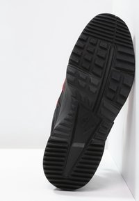 Musta kuminen lenkkarituki, jossa on kuvioitu pito ja hienovarainen urastus sekä selkeä logon yksityiskohta. Sivulla näkyy punaiset korostukset.