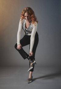 Stříbrné podpatky se špičatými prsty a šněrováním, v kombinaci s černými kalhotami. Modelka má texturované dlouhé rukávy a protézu nohy.