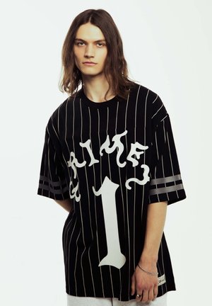La camiseta oversized de rayas negras presenta un gran texto gráfico en blanco "PRIME" y el número "1", con acentos de rayas grises en las mangas. Tejido suave.
