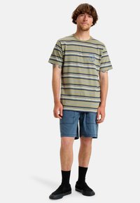 Striped short-sleeve t-shirt in olive green and navy. Features a crew neckline and a small logo on the chest. Paired with blue shorts and black socks.