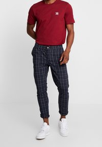 Camiseta de algodón roja con mangas cortas y logo blanco, combinada con pantalones de cuadros en azul marino y zapatillas blancas, con botón y puños.