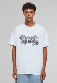 Hvid bomulds t-shirt med en sort graffiti-lignende "NEW YORK" grafik centreret på forsiden, med løse ærmer og rund halsudskæring.