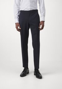 Marineblaue Anzughosen mit maßgeschneiderter Passform, glatter Textur, Seitentaschen und Knopfdetails am Bund. Kombiniert mit schwarzen Dressschuhen.