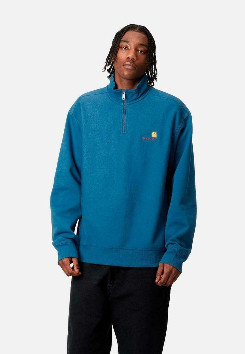 Sudadera de forro polar azul con media cremallera, puños acanalados y un pequeño logo en el pecho. Presenta un ajuste clásico y relajado, con una textura suave.