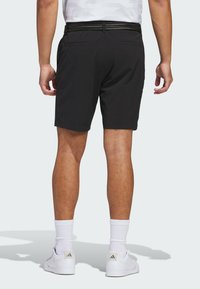 Svarta shorts med en texturerad midja, bakfickor och rak skärning, ihop med vita sneakers och strumpor. Ren, minimalistisk design.