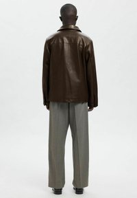 Rjava usnjena jakna z ohlapnim krojem, velikim ovratnikom in gumbi na manšetah. Kombinirana z zeleno-sivimi širokimi hlačami in črnimi čevlji.