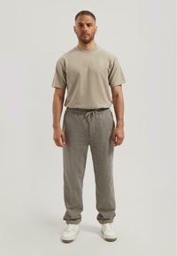 Beige katoenen t-shirt gecombineerd met een losvallende broek met ruiten in grijs en bruin. Witte sneakers maken de outfit af.