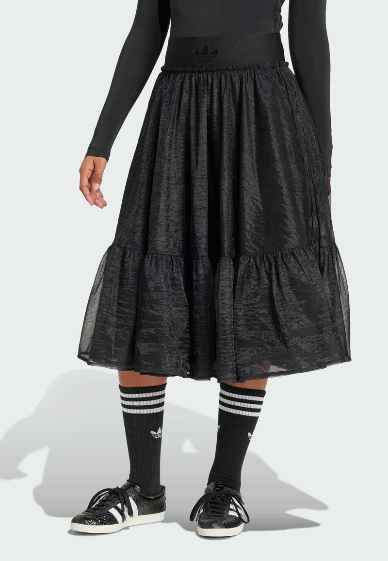 Black tiered skirt made of textured fabric, featuring an elastic waistband and a subtle sheen, paired with striped black socks and black sneakers.