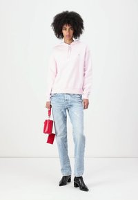 Felpa con cappuccio rosa chiaro, jeans azzurri chiari strappati, stivali neri con tacco alla caviglia e una piccola borsa rossa con tracolla.