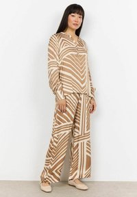 Gestreiftes Zweiteiler-Outfit in Tan und Cremetönen, bestehend aus einem geknöpften V-Ausschnitt-Oberteil und weit geschnittenen Hosen, die elastische Bündchen und eine weiche Stofftextur aufweisen.