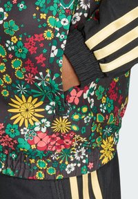 Φλοράλ μπουφάν με μαύρη βάση και πολύχρωμα ανθισμένα μοτίβα, ελαστικές μανσέτες και χρυσές ρίγες δίπλα στις τσέπες.