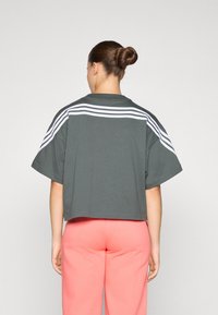 Κοντομάνικo γκρι T-shirt με ψηλή μέση και τρεις λευκές ρίγες στο πίσω μέρος. Συνδυάζεται με ροζ παντελόνι, με απλή υφή και χαλαρή εφαρμογή.