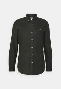 Ciemnozielona koszula z sztruksu z długimi rękawami, kołnierzykiem na guziki, białymi guzikami i małym żółtym logo po lewej stronie klatki piersiowej.