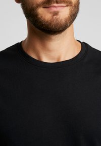Black T-shirt featuring a round neckline, short sleeves, and a smooth, cotton texture. No visible patterns or accents.