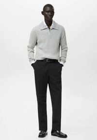 Pulover gri deschis din tricot cu dungi, cu guler polo, asortat cu pantaloni negri cu talie înaltă și pantofi negri din piele. Design simplu cu texturi contrastante.