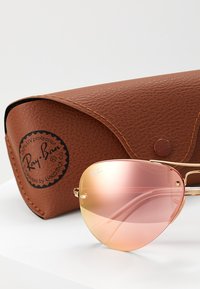 Óculos de sol Ray-Ban com uma armação de metal dourado e lentes em gradiente rosa. Inclui uma cela de couro castanho texturizado com o logótipo da marca.
