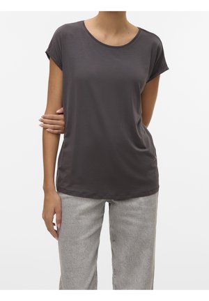 Frau mit kurzärmligem dunkelgrauem T-Shirt und hellgrauer Jeans, die mit einem Arm um die Taille steht.