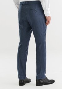 Spodnie w marynarskim wzorze o dopasowanym kroju, z mikro-rąbkiem, z pętelkami na pasek i dwiema tylnymi kieszeniami, w zestawieniu z czarnymi butami.