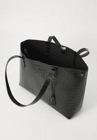 Sac fourre-tout en crocodile noir embossé avec texture lisse, deux poignées supérieures et un accent de verrou. Intérieur ouvert avec un design minimaliste.