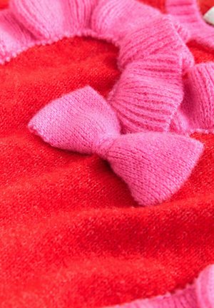 Červená pletená tkanina s jemnou textúrou, ozdobená ružovým nariaseným lemom a dvoma ružovými pletenými mašľami. Dizajn je bezšvový a žiarivý.