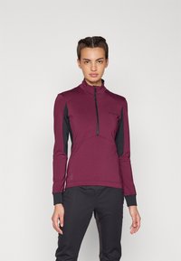 Haut à manches longues bordeaux avec un col montant, fermeture éclair mi-haut à l'avant, et panneaux latéraux noirs ; fabriqué en tissu extensible avec une texture lisse.