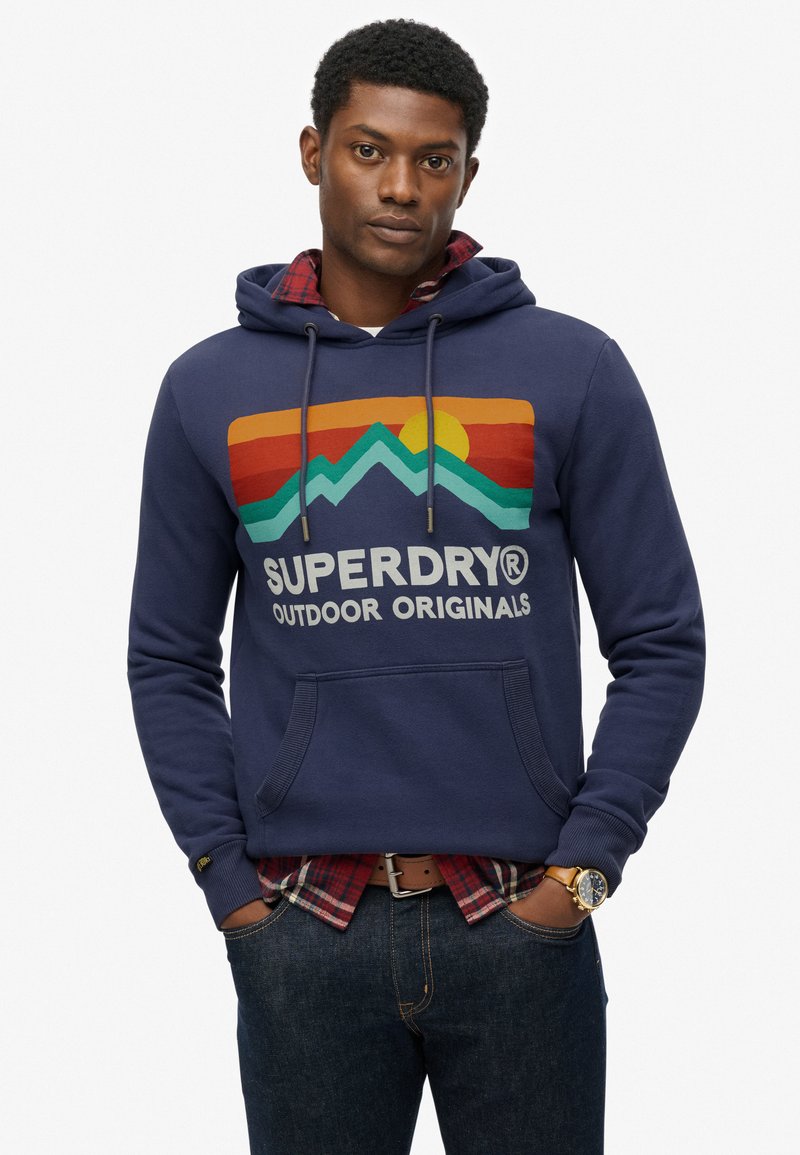 Marineblauwe hoodie van een katoenmix met een grafisch ontwerp van bergen en de zon aan de voorkant, een capuchon met trekkoord en een kangoeroezak, gecombineerd met een geruite shirt.