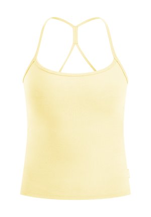 Kvinde iført en lys gul tætsiddende tanktop og leggings med hvide træningssko, stående med hænderne bag ryggen.