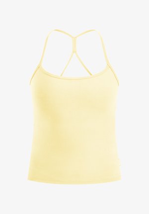 Vrouw die een lichtgele aansluitende tanktop en legging draagt met witte sportschoenen, staand met haar handen achter haar rug.