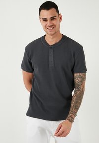 Maglietta henley grigio scuro a maniche corte con tessuto testurizzato, patta con tre bottoni e design del colletto tondo.