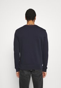 Felpa blu navy con maniche lunghe, polsini e orlo a coste. La scollatura posteriore presenta una cucitura rossa. Il tessuto sembra liscio e morbido.