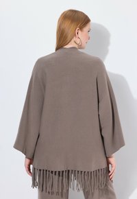Cardigan marrón con flecos, fabricado en un tejido texturizado, con frente abierto y mangas anchas. Diseñado para un ajuste relajado.