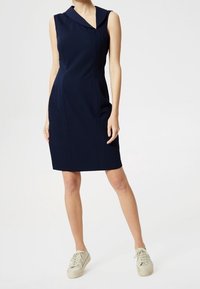 Námořnické bezrukávové šaty s přehnutým límcem, bočními švy a přiléhavým střihem, doplněné světle zbarvenými teniskami.