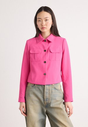 Veste courte rose avec un col, deux poches poitrine et cinq boutons marron. Portée avec un jean baggy bleu clair.