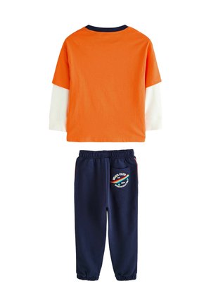 Ensemble deux pièces comprenant un haut court à manches courtes orange avec un panneau blanc et un pantalon de jogging bleu marine avec une poche accentuée et un logo.