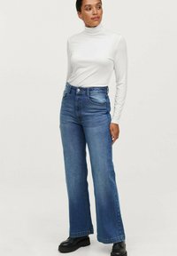 Højtaljede blå denim jeans med lige ben, der har fem lommer, synlige syninger og en klassisk knaplukning.