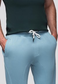 Pantalones deportivos azul claro con cintura elástica y cordón blanco, que presentan bolsillos laterales y un acabado de textura suave.