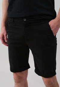 Shorts noirs en coton avec un ourlet roulé, dotés d'une fermeture à bouton sur le devant, de poches latérales et d'une texture lisse.