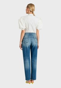 Blusa bianca a righe verticali con maniche a palloncino, abbinata a jeans blu a vita alta. Modella che indossa sandali gialli con tacco, vista da dietro.