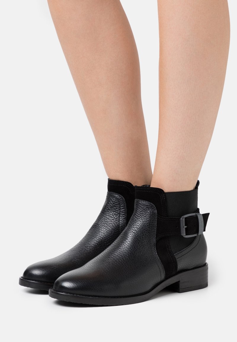 Botas negras hasta el tobillo hechas de cuero texturizado con paneles elásticos y una hebilla decorativa en el costado. Tacón plano y acabado suave.
