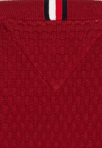 Red knitted sweater featuring a textured pattern, with a V-shaped neckline and a striped accent in red, white, and black at the collar.