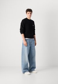 Zwarte gebreide trui met een klein logo, gecombineerd met lichtblauwe wijde jeans en witte sneakers. Eenvoudig ontwerp, casual pasvorm, textuurstof.