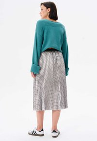 Turquoise gebreide trui met oversized manchetten, gecombineerd met een geplooide midi rok met een geometrisch zwart-wit patroon en witte sneakers.