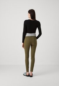 Top negro de manga larga con cintura gris, combinado con pantalones ajustados verde oliva. El modelo lleva zapatillas de lona azul claro.